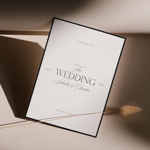 Pu&ograve; includere: Un invito di nozze con bordo nero, con il testo "WELCOME TO The WEDDING Juliette & Charles 2026" e la data "AUG 1". Viene visualizzata anche la localit&agrave; "VENICE, ITALY". L'invito &egrave; su sfondo bianco.