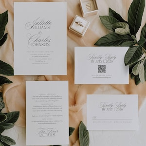 May include: Elegant wedding invitation suite with white cards featuring black calligraphy. The suite includes an invitation, RSVP cards, and details card. A ring box and a ring are also visible, along with green leaves.