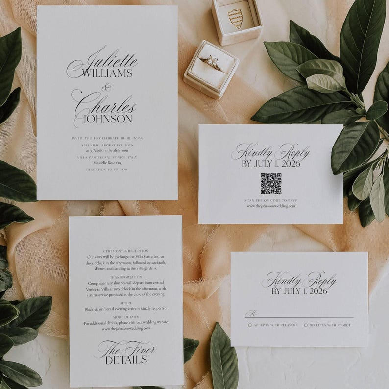 May include: Elegant wedding invitation suite with white cards featuring black calligraphy. The suite includes an invitation, RSVP cards, and details card. A ring box and a ring are also visible, along with green leaves.