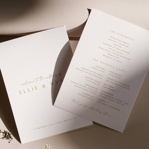 Op de afbeelding: Twee elegante trouwprogramma's met gouden tekst op een witte achtergrond. Het linkerprogramma leest "welcome to the wedding of ELLIE & RYA" en de datum. Het rechterprogramma vermeldt de ceremonie en de details van de bruiloft.