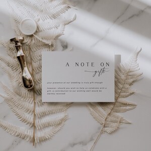 Op de afbeelding: Een witte kaart met de tekst "A Note On Gifts" in zwarte letters. De tekst eronder luidt: "Uw aanwezigheid op onze bruiloft is al een cadeau op zich. Mocht u ons echter willen helpen met het vieren van onze dag met een cadeau, dan is een bijdrage in onze wensbox van harte welkom."