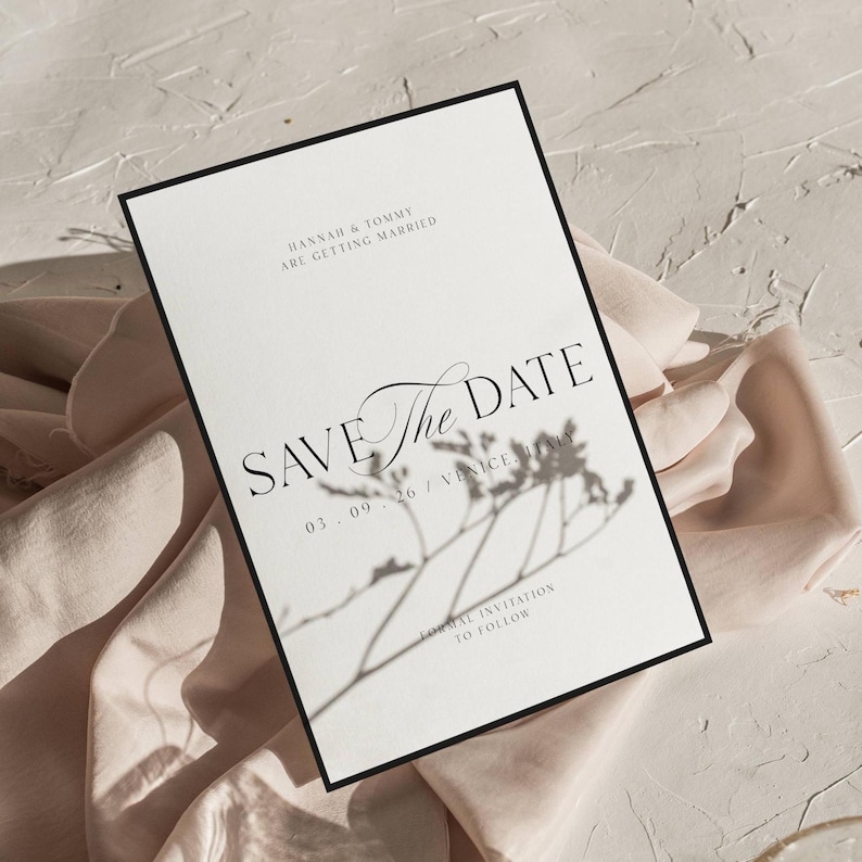 May include: A white Save the Date card with a black border. The card features elegant script and text that reads "HANNAH & TOMMY ARE GETTING MARRIED" and "SAVE THE DATE". A shadow of a plant is cast on the card.