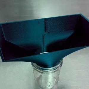 May include: A dark teal 3D printed funnel with a wide opening and a narrow spout, positioned over a clear glass jar.