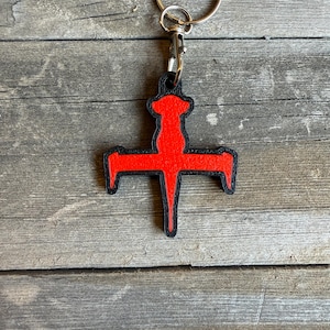 May include: A red and black keychain with a stylized cross design. The keychain is attached to a silver key ring.