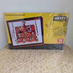 Puede incluir: Set de figuras de lujo coleccionables con Mickey Mouse. El set incluye m&uacute;ltiples figuras de Mickey Mouse en varias poses. El embalaje es amarillo y negro, con el texto "Mickey The True Original" y "90 Years of Magic".