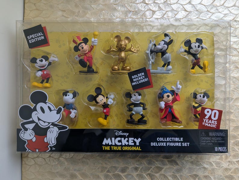 Puede incluir: Un juego de figuras de lujo coleccionables con diez figuras de Mickey Mouse en varias poses y atuendos. El juego incluye una figura dorada de Mickey y celebra 90 a&ntilde;os de magia. Las figuras se exhiben en un paquete de pl&aacute;stico transparente.