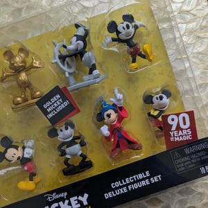 Puede incluir: Un juego de figuras de lujo coleccionables con varias figuras de Mickey Mouse. El juego incluye un Mickey Mouse dorado, Mickey como capit&aacute;n y Mickey en varias poses. El embalaje incluye el texto "90 Years of Magic" y "The True Original."