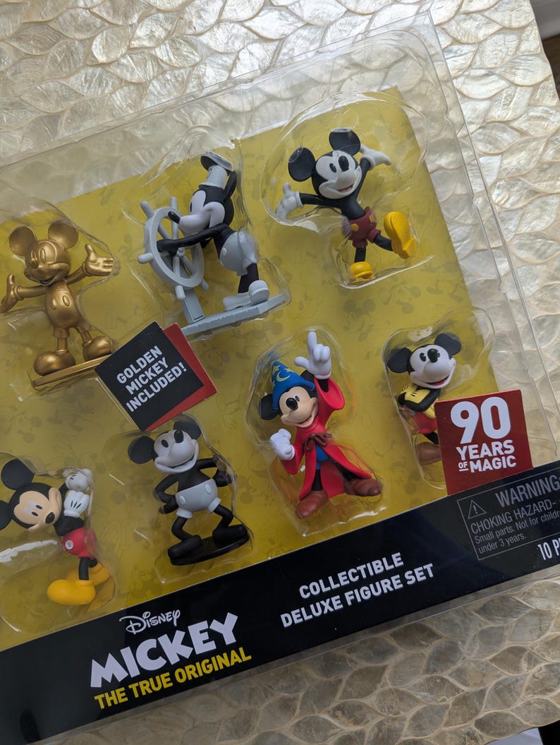 Puede incluir: Un juego de figuras de lujo coleccionables con varias figuras de Mickey Mouse. El juego incluye un Mickey Mouse dorado, Mickey como capit&aacute;n y Mickey en varias poses. El embalaje incluye el texto "90 Years of Magic" y "The True Original."