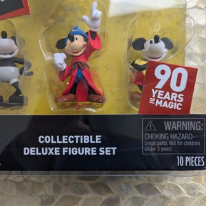 Puede incluir: Set de figuras de lujo coleccionables con tres figuras de Mickey Mouse. Una figura es en blanco y negro, otra est&aacute; vestida de hechicero y la tercera lleva un atuendo amarillo y rojo. El embalaje incluye una pegatina "90 Years of Magic".