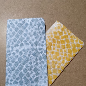 Peut inclure: Deux feuilles de papier de soie à motifs. L'une est bleue avec un motif en losange blanc et l'autre est jaune avec un motif en losange blanc.
