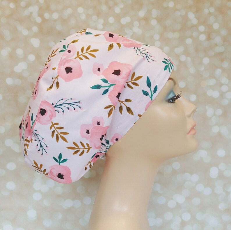 May include: A pink scrub hat with a floral pattern featuring pink flowers, green leaves, and gold stems.