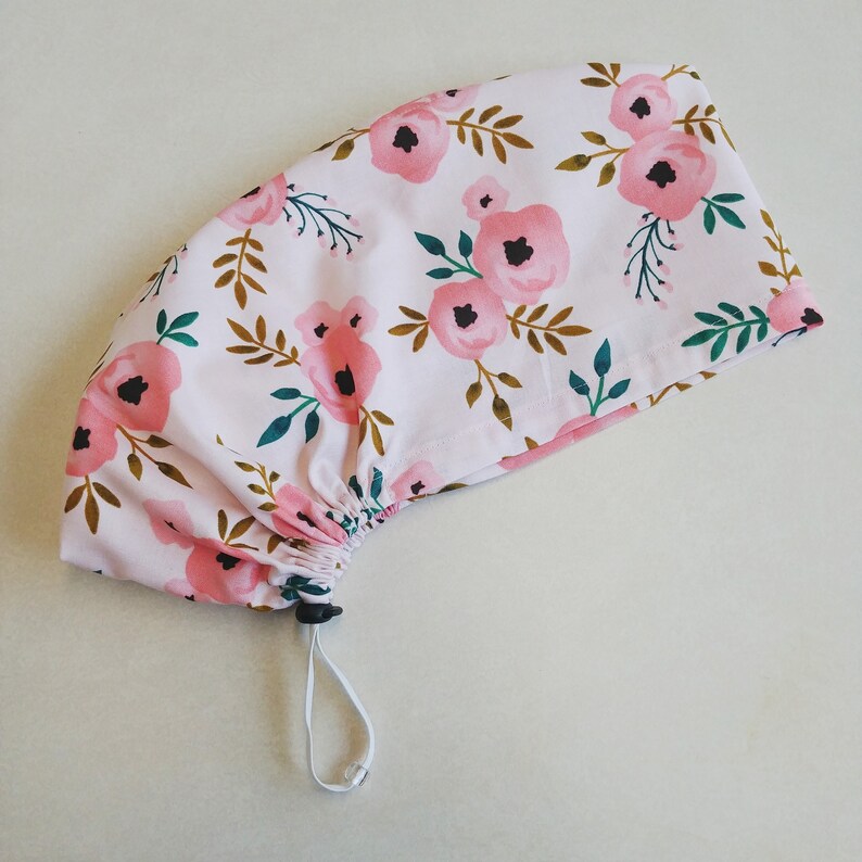 May include: A pink drawstring bag with a floral pattern featuring pink flowers and green leaves. The bag has a white drawstring.