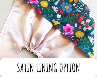 May include: A pink satin lined hat with a green floral print featuring butterflies, mushrooms, and flowers. The text "SATIN LINING OPTION" is printed on a white label below the hat.
