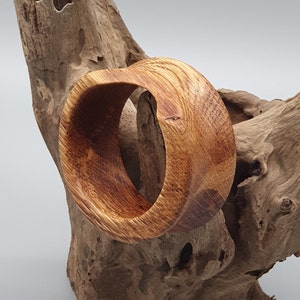 May include: A wooden bangle with a natural brown finish. The bangle is made from a single piece of wood and has a smooth, polished surface.