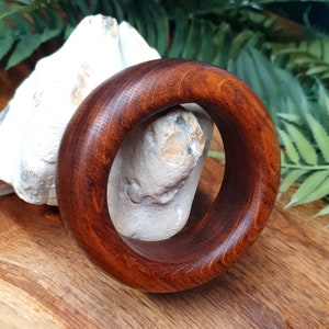May include: A dark brown wooden bangle with a smooth, polished finish. The bangle is thick and has a rounded shape.