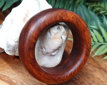 May include: A dark brown wooden bangle with a smooth, polished finish. The bangle is thick and has a rounded shape.