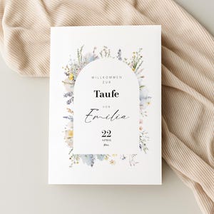 Könnte beinhalten: Eine weiße Einladungskarte mit floralen Akzenten. Die Karte zeigt ein bogenförmiges Design mit den Worten "Willkommen zur Taufe von Emilia" und dem Datum "22 April". Das Blumenarrangement enthält Pastellfarben.