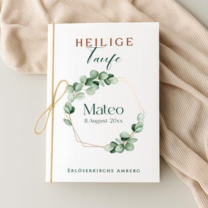 Könnte beinhalten: Eine weiße Einladungskarte mit den Worten "HEILIGE Taufe" in Burgunderrot und türkisblauer Schrift. Die Karte zeigt einen Aquarell-Eukalyptus-Kranz um den Namen "Mateo" und das Datum "11.August 20xx". Der Kirchenname "ERLÖSERKIRCHE AMBERG" steht unten. Eine Schnurschleife sichert die Karte.