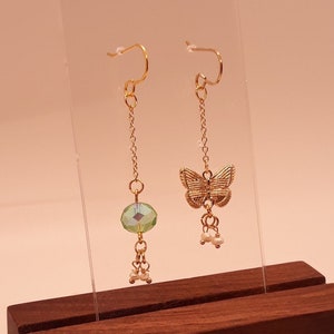 Peut inclure: Une paire de boucles d'oreilles pendantes dorées avec une perle de cristal verte et un charme papillon sur une boucle d'oreille et une perle de cristal verte et trois petits charmes de perles sur l'autre boucle d'oreille.
