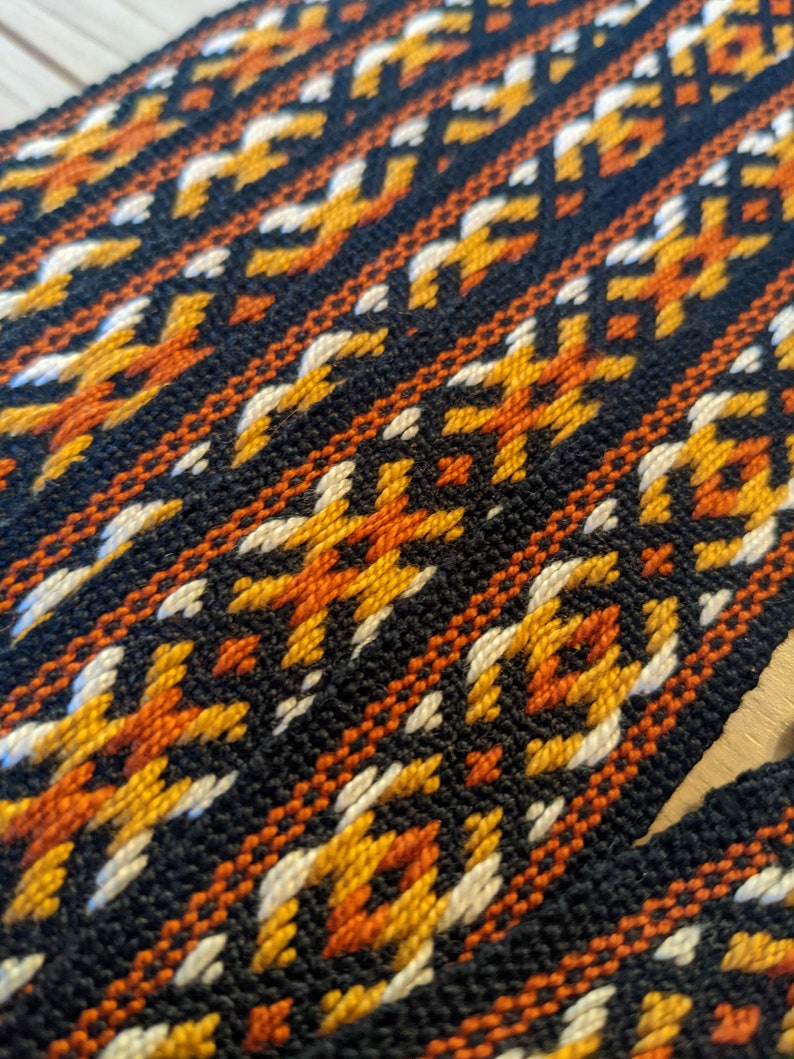 May include: Close-up of a woven fabric with a geometric pattern in black, orange, white, and yellow.