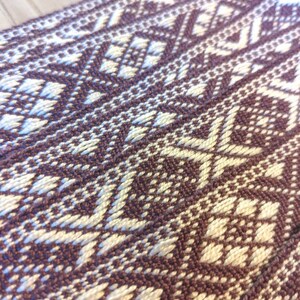 May include: Close-up of a woven fabric with a geometric pattern in shades of brown and white.