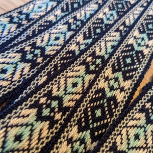May include: Close-up of woven black, cream, and light green fabric with a geometric pattern. The fabric is folded in layers, showing the pattern repeating.