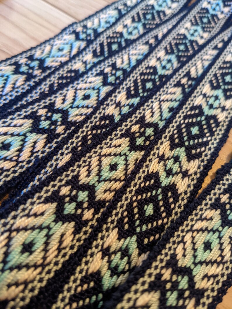 May include: Close-up of woven black, cream, and light green fabric with a geometric pattern. The fabric is folded in layers, showing the pattern repeating.