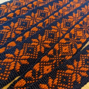 May include: Close-up of woven fabric with a repeating pattern of orange and dark blue geometric shapes.