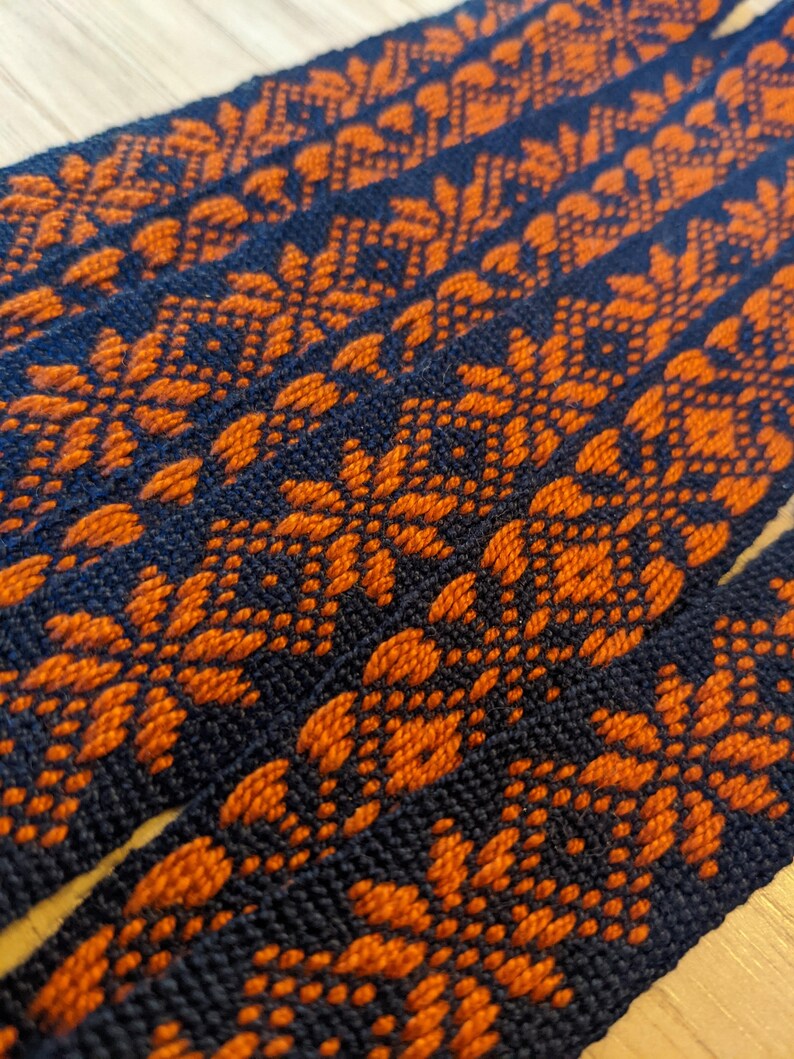 May include: Close-up of woven fabric with a repeating pattern of orange and dark blue geometric shapes.