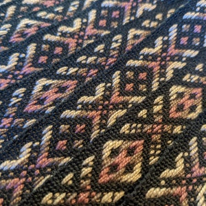 May include: Close-up of a woven fabric with a geometric pattern in shades of black, brown, and pink.