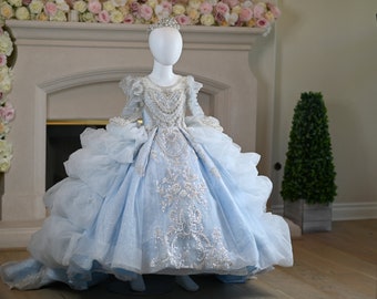 May include: A light blue tulle ball gown with silver embroidery and beading. The dress has a long train and is on a mannequin.