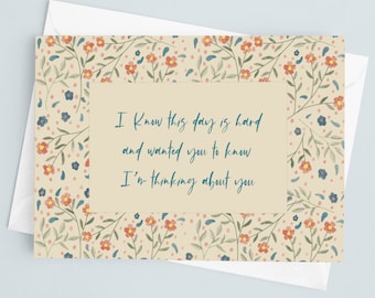 Puede incluir: Tarjeta de condolencia con diseño floral. La tarjeta tiene un fondo beige con un patrón floral de flores rojas, azules y amarillas. El texto dice: "Sé que este día es duro y quería que supieras que estoy pensando en ti."