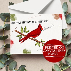 May include: A birthday card featuring a red cardinal perched on a branch with green leaves. The card reads "Hope your birthday is a tweet one" and "Happy Birthday." The card is printed on canvas linen paper.
