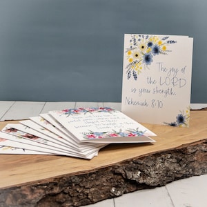 May include: A stack of blank greeting cards with floral designs and inspirational quotes. The top card features a watercolor floral design with the quote "The joy of the LORD is your strength. Nehemiah 8:10".