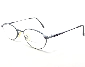 May include: A pair of silver-toned metal eyeglasses with oval-shaped lenses. The frames have a textured design on the arms.