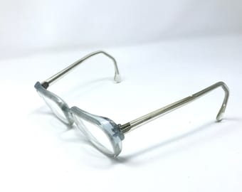 May include: Clear-framed eyeglasses with silver-toned arms. The lenses are clear, and the frames have a subtle, light blue tint. The glasses are set against a white background, showcasing their design and style.