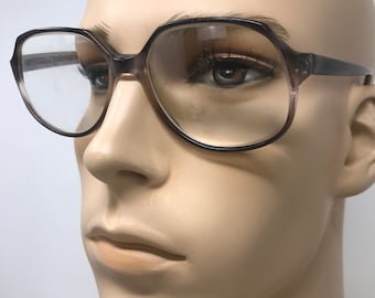 May include: Close-up of vintage eyeglasses with a geometric frame. The glasses have a dark brown frame with a gradient of light brown and clear lenses. The glasses are displayed on a mannequin head.