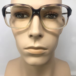 Peut inclure: Lunettes vintage à monture carrée. Les montures présentent un dégradé de couleurs, allant du noir au violet, puis au jaune clair. Les verres sont transparents. Les lunettes sont présentées sur une tête de mannequin.