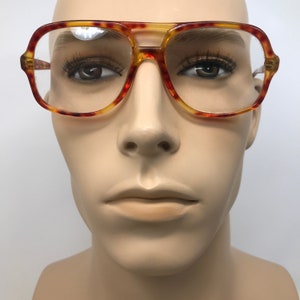 May include: Vintage eyeglasses with a tortoiseshell pattern. The frames are a combination of amber, red, and yellow hues. The lenses are clear, and the glasses have a classic aviator shape.