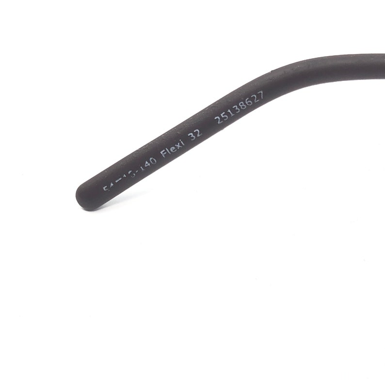 May include: A close-up of a dark gray eyeglass arm with the text "54-15-140 Flexi 32" and the number "25138627" printed on it. The arm is curved and has a rounded tip.