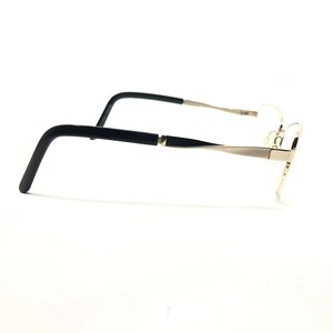 Pu&ograve; includere: Un paio di occhiali con montatura in metallo color oro e aste nere. Gli occhiali sono mostrati di profilo su sfondo bianco. Le aste hanno una forma rettangolare e sono collegate alla montatura con una piccola cerniera.