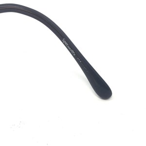 May include: Close-up of a black eyeglass arm with the text "Specsavers" printed in white. The arm curves slightly and ends in a rounded tip. The background is white.