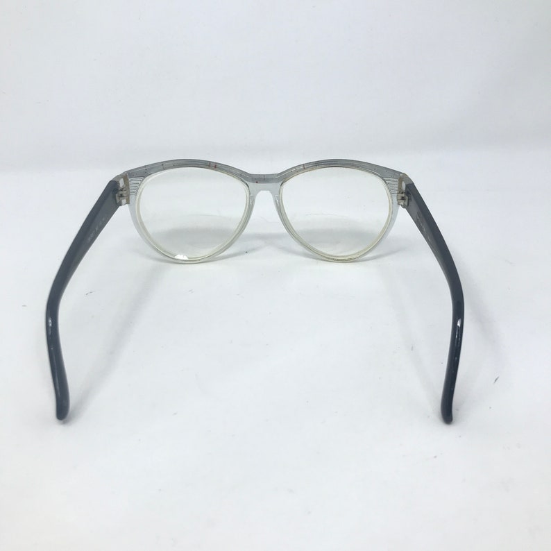 May include: A pair of silver-rimmed eyeglasses with black plastic arms. The glasses have a round shape and clear lenses.