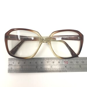 May include: Brown and clear eyeglasses with a rectangular shape. The glasses have a gradient tint and are measured with a ruler. The frame has the text "SPECSAVERS 175428" and "DEN 21063732".