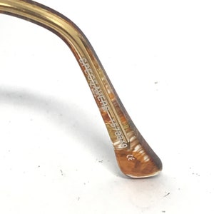 May include: Close-up of the arm of eyeglasses. The arm is a marbled brown and tan color. The text "SPECSAVERS" and "5738F0" is printed on the arm. The end of the arm has a small "CE" marking.
