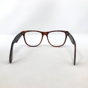 May include: Eyeglasses with a classic rectangular frame in a tortoiseshell pattern. The temples are dark brown and extend outward. The lenses are clear. The glasses are set against a white background.
