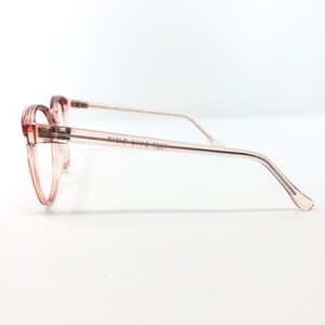 May include: Pale pink eyeglasses with a rounded frame and thin temples. The glasses have a transparent frame and arms, with the text "FABIO CONTI 3227" printed on the temple. The glasses are set against a white background.