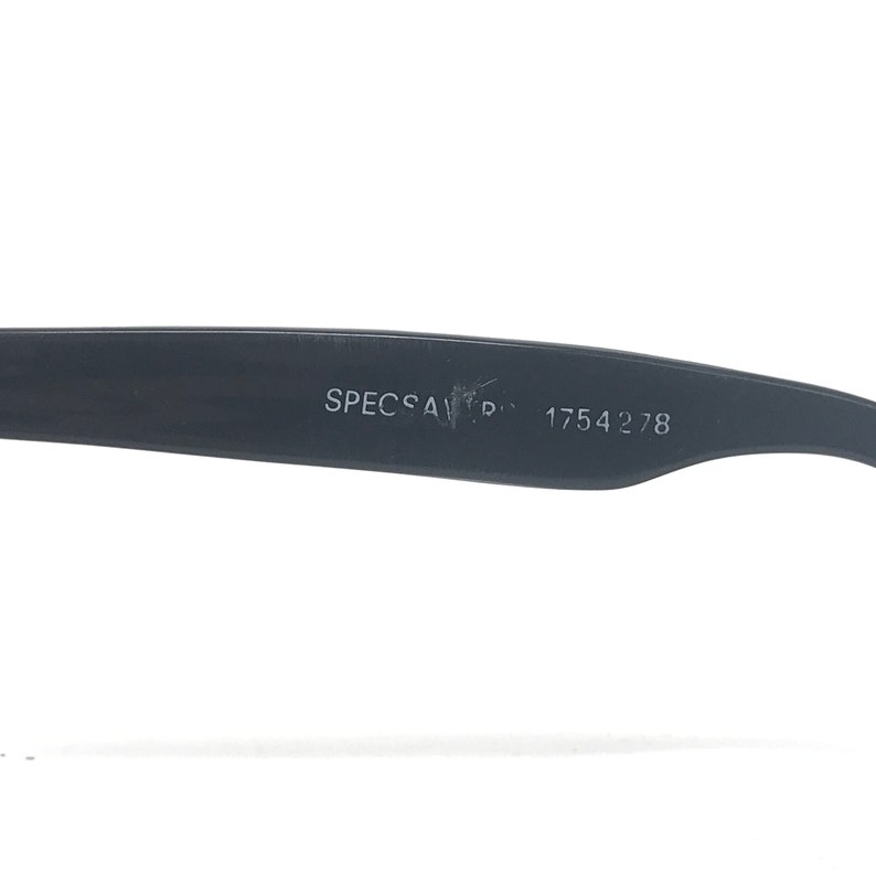 May include: Close-up of a black eyeglass frame arm with the text "SPECSAVERS" and the number "1754278" printed in white. The frame is made of a matte black material.
