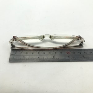 May include: Transparent-framed spectacles with a metal and plastic construction. The glasses are measured with a ruler, showing a length of approximately 13 cm. The lenses are clear, and the frame has a subtle brown tint.