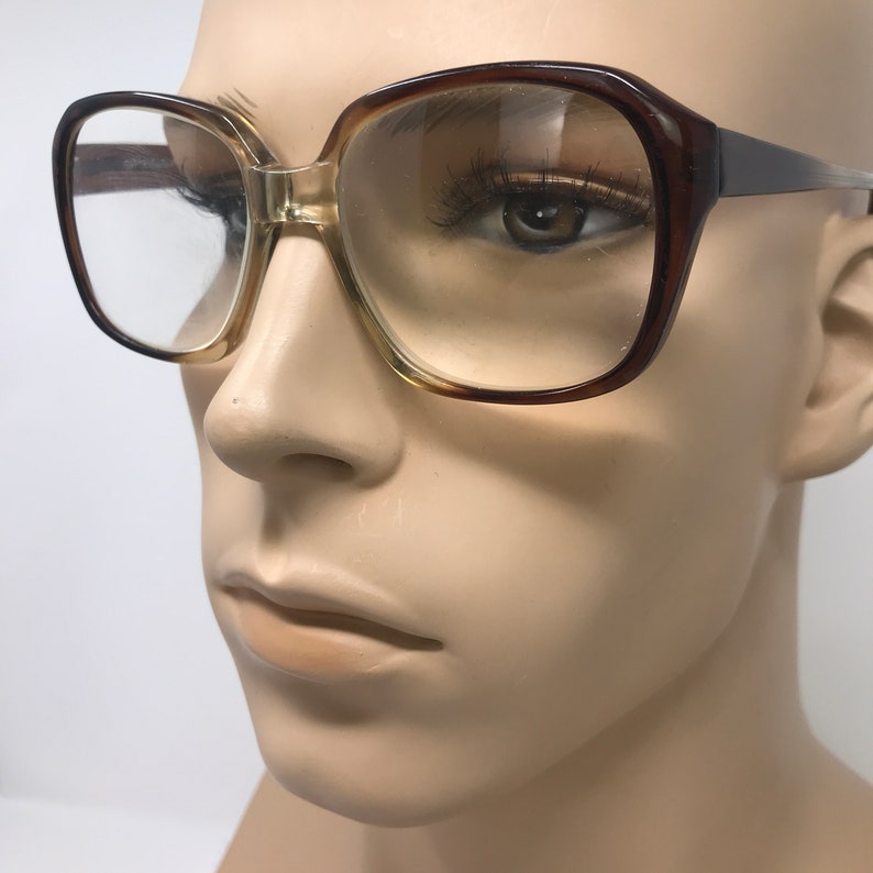 May include: Vintage square-framed eyeglasses with a gradient brown and clear design. The frames have a thick, retro style, with a light brown gradient on the lower half of the lenses and a darker brown on the upper half. The glasses are displayed on a mannequin.